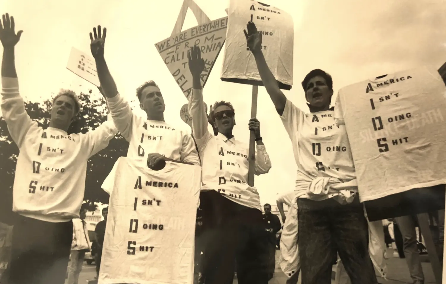 People protesting for recognition of AIDS with signs that read “America Isn’t Doing S—-“