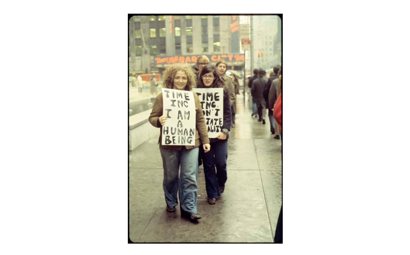 Protesters picketing, one visible sign says 'Time Inc. I am a human being'