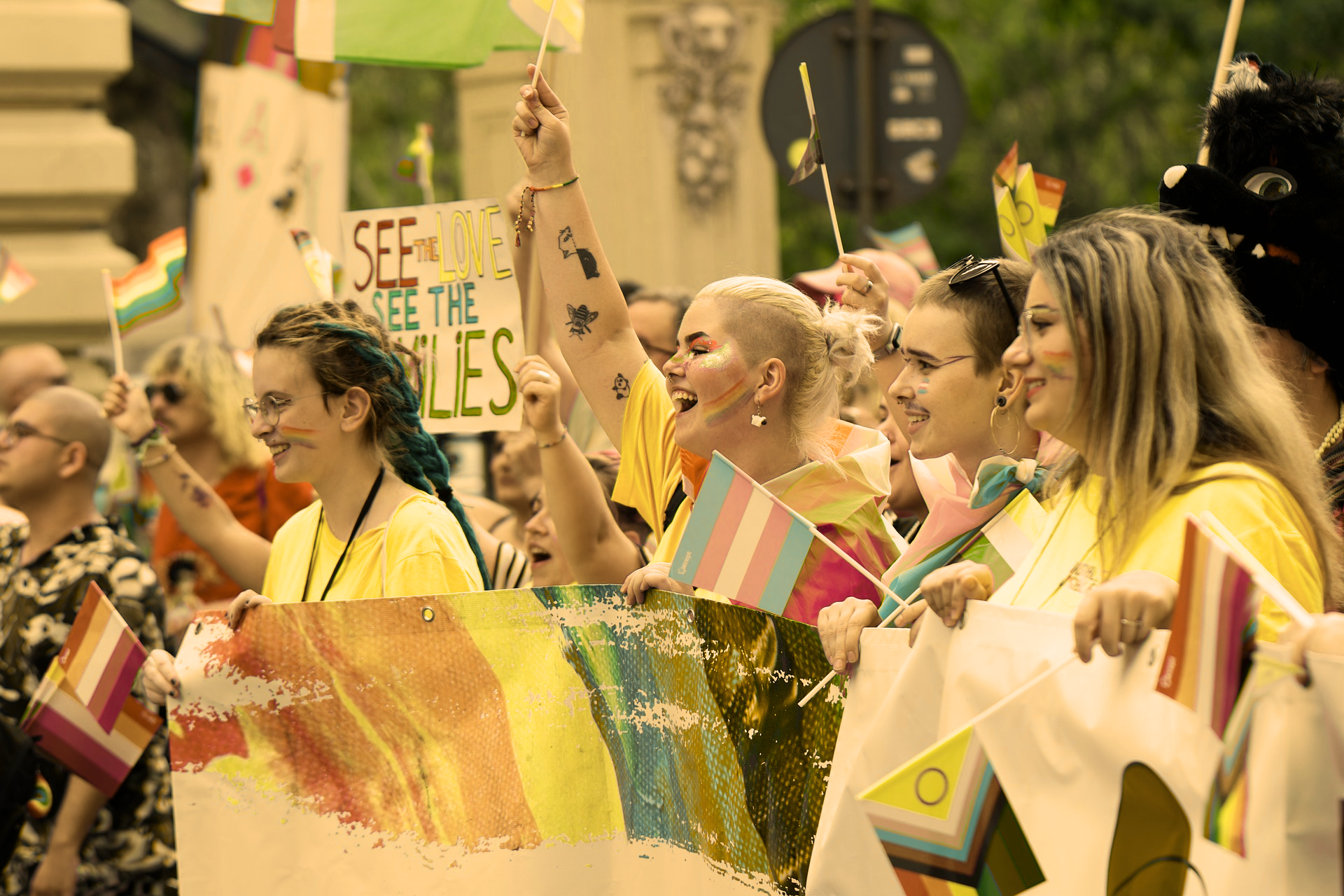 Yellow tinted image that shows a crowd at pride holding flags and posters